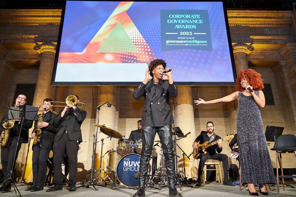 Vocalists and horn section performing under stage lights